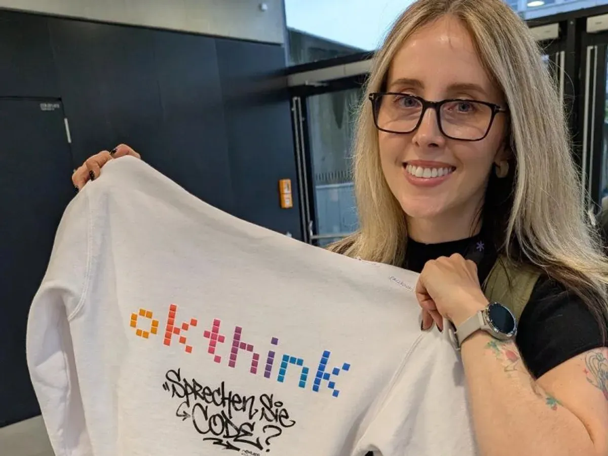 Margaret holding up a white okthink sweatshirt printed with the okthink wordmark and the words Sprechen Sie Code